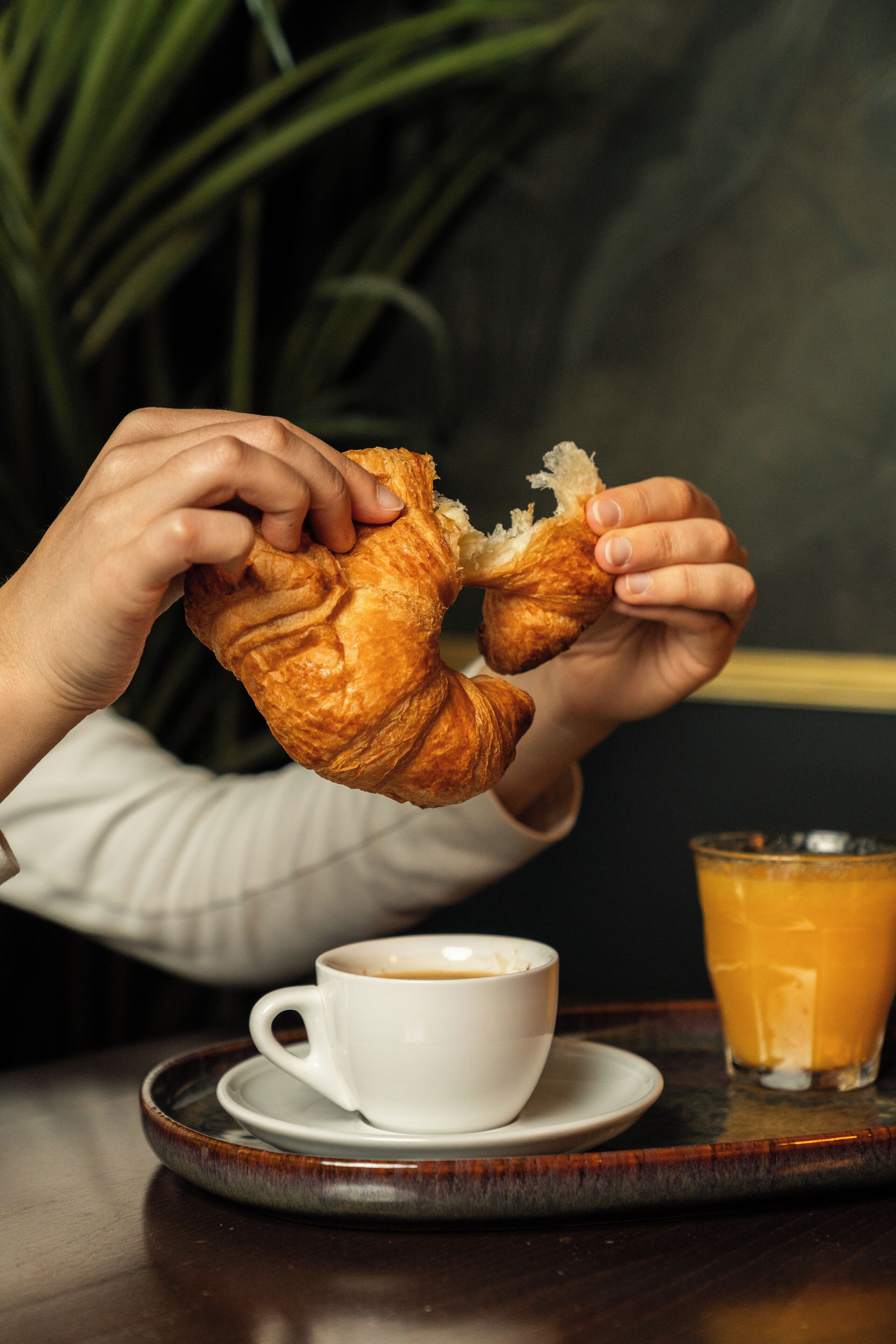 A person holding a croissant, a cup of coffee, and a glass of orange juice on a tray.