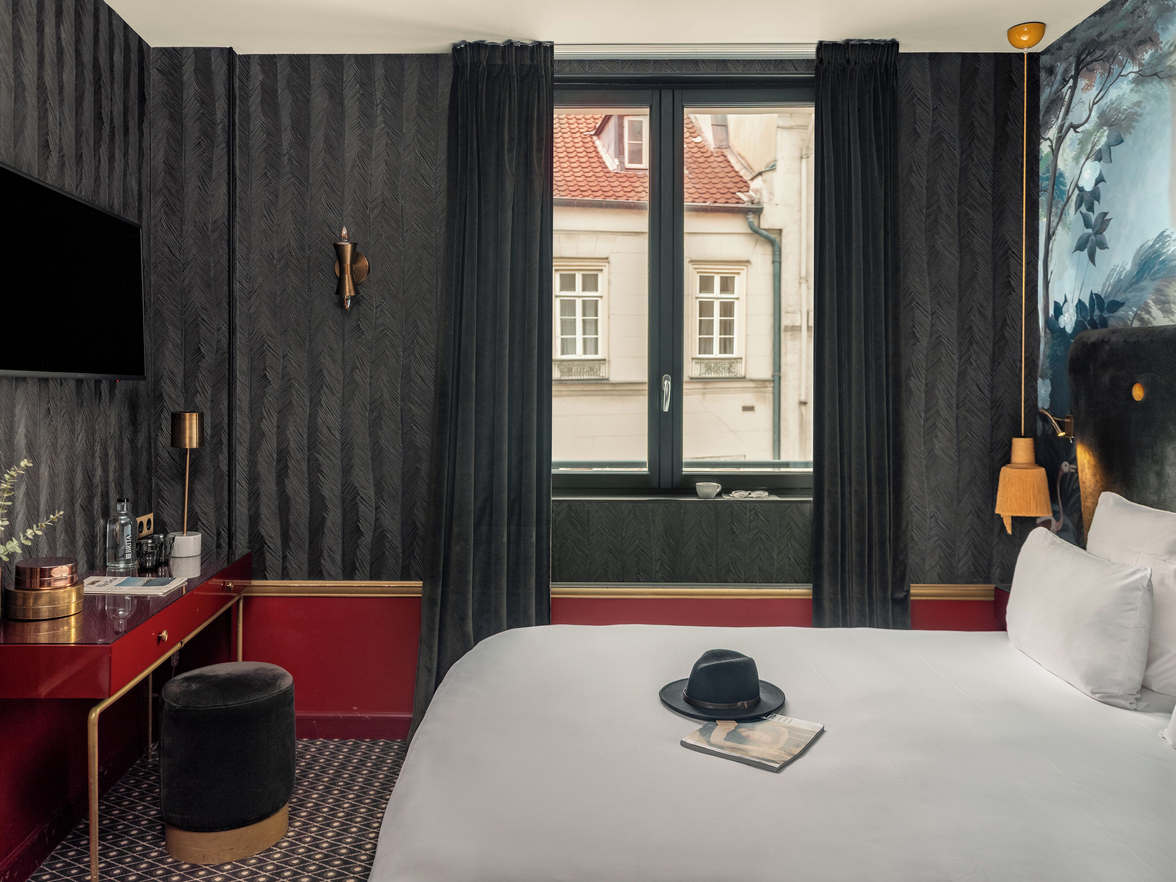 A hotel room with a bed, a desk, a chair, a TV, a window with curtains, and a painting on the wall.