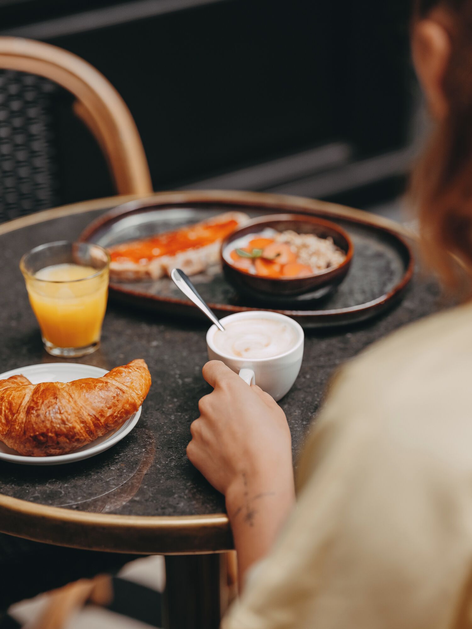 A dining table with a croissant, a bowl of soup, a glass of orange juice, and a cup of coffee.