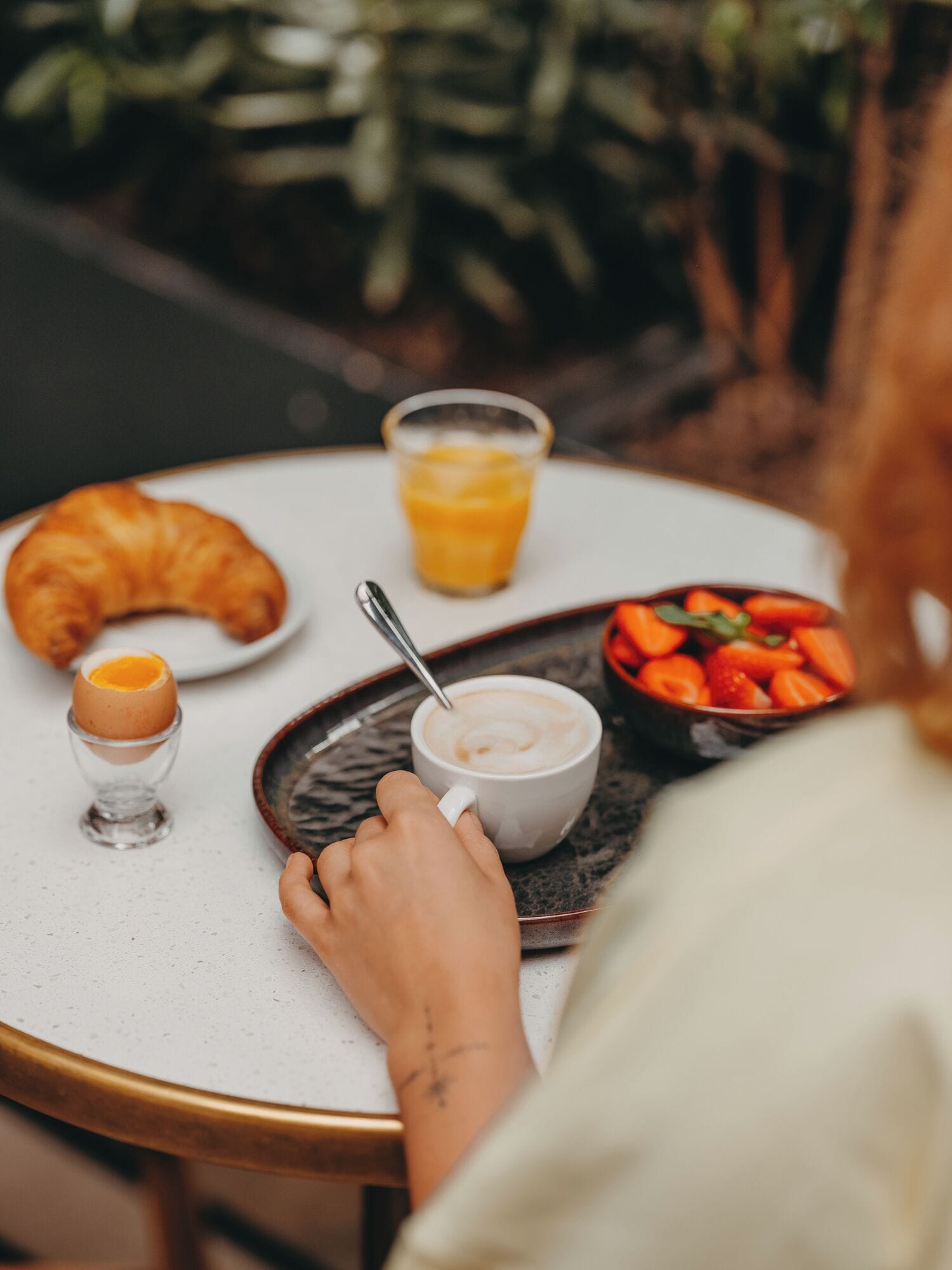 Ein Frühstücksbuffet mit einem Croissant, einer Tasse Kaffee, einem Glas Orangensaft und einer Schale Erdbeeren auf einem runden Tisch.