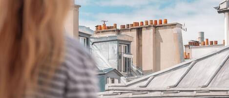 A person standing on a balcony overlooking a cityscape with buildings and a clear sky.
