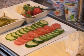 Un bufé con rodajas de pepino, tomates y un bol de fresas.