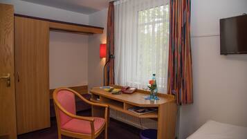 Una habitación de hotel con un escritorio de madera, una silla, una cama, un televisor y una ventana con cortinas.