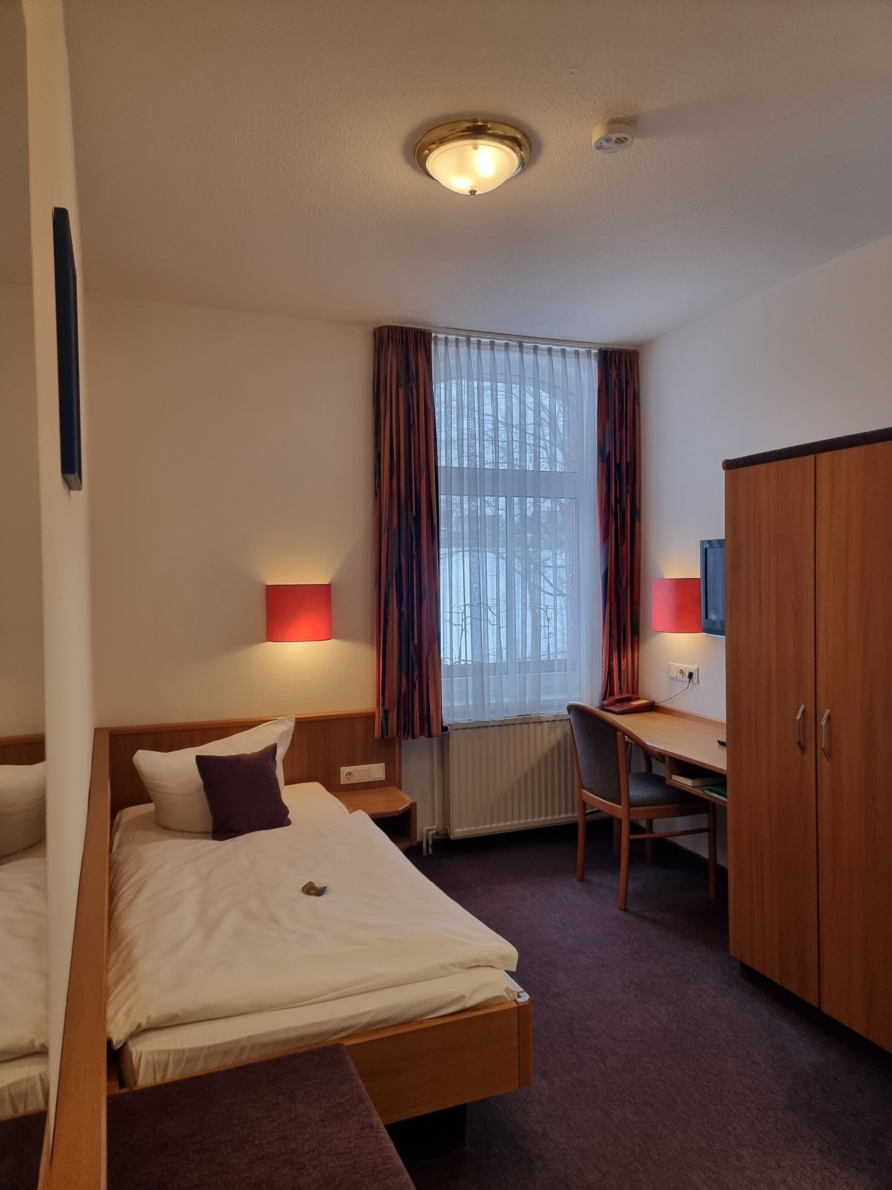 A hotel room with two beds, a desk, a chair, a wardrobe, and a window with curtains.