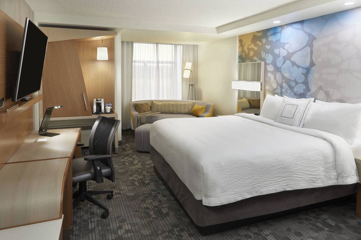 Une chambre d’hôtel avec un grand lit, un bureau avec un ordinateur, une chaise, un canapé et une télévision.