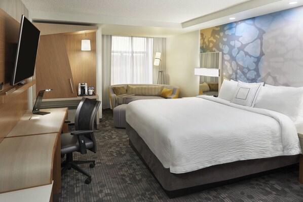 Habitación de hotel con una cama grande, un escritorio con computadora, una silla, un sofá y un televisor.
