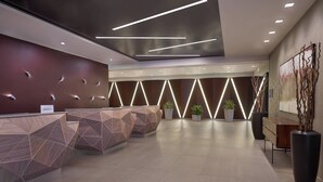 A modern reception area with geometric patterned reception desks, recessed lighting, and a large abstract painting on the wall. - Courtyard by Marriott Oshawa (Oshawa)