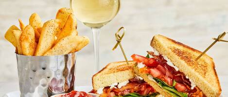 Un sándwich con papas fritas y una copa de vino blanco en un plato.
