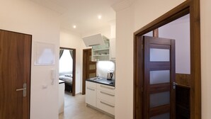 Un couloir étroit donnant sur une chambre, avec un lit, un coin cuisine et une porte menant à une autre pièce.