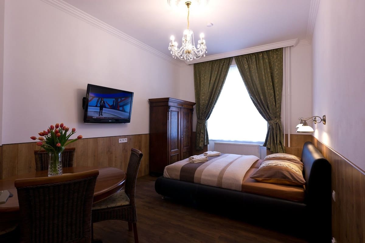 Une chambre d’hôtel comprenant un lit, une télévision, une table à manger avec des chaises, un vase de fleurs et un lustre.