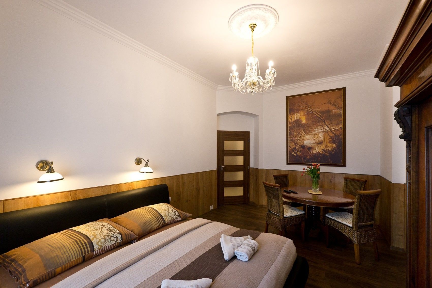 Camera d'albergo con un letto, lampade sui comodini, un lampadario, un tavolo da pranzo con sedie e un quadro appeso al muro.