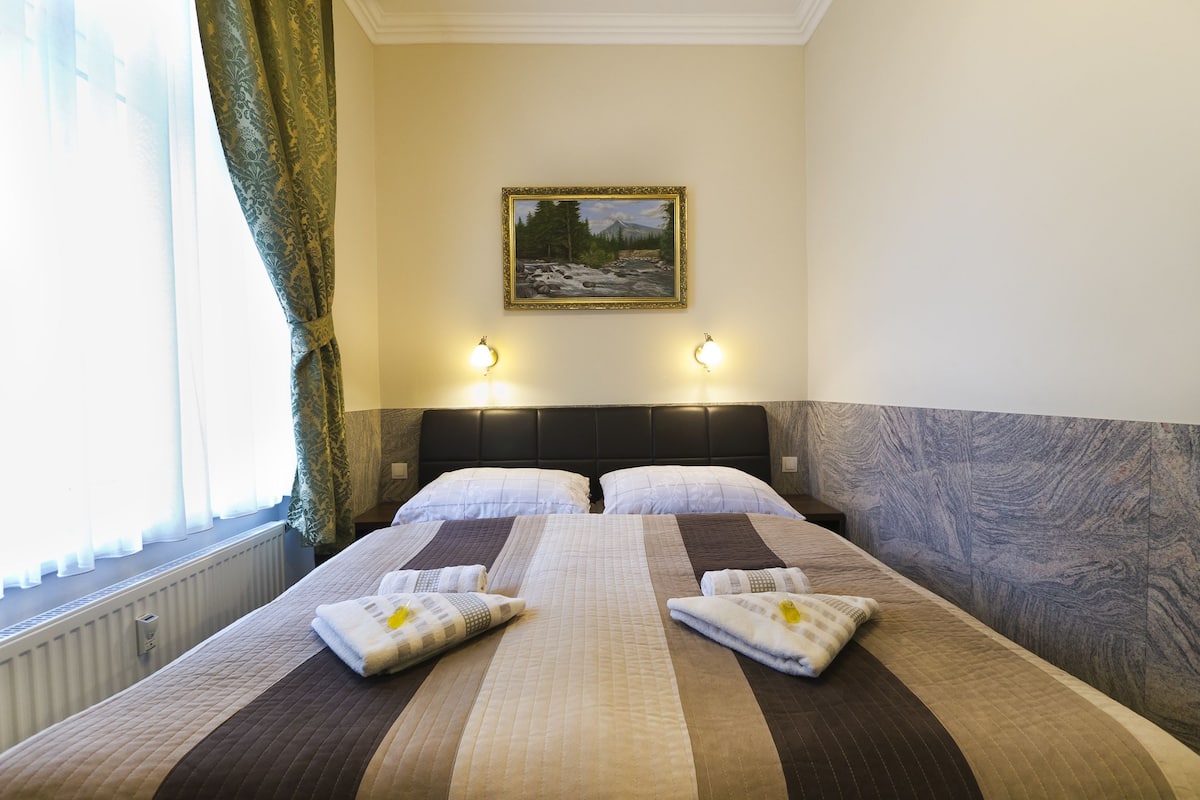 Une chambre d’hôtel avec un grand lit, deux lampes de chevet, un tableau au mur et une fenêtre avec des rideaux.