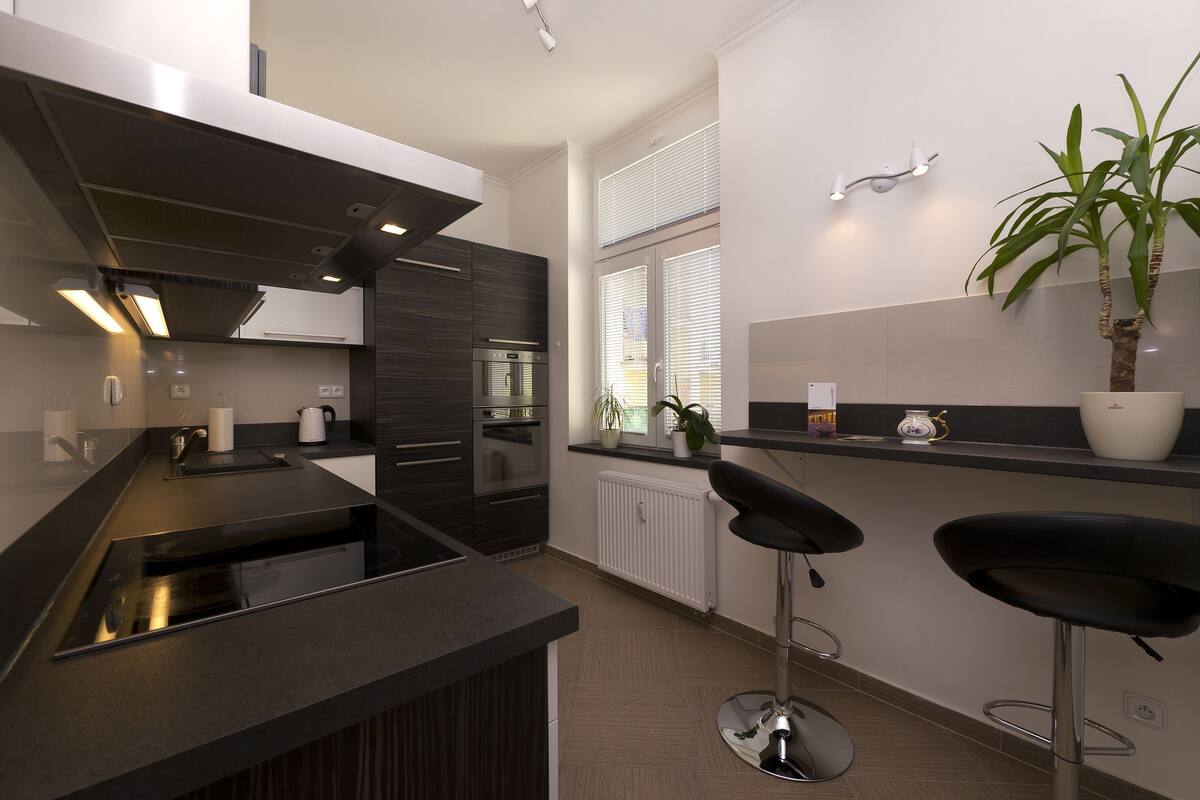 Une cuisine moderne avec des meubles de couleur sombre, un plan de travail noir et deux tabourets de bar.