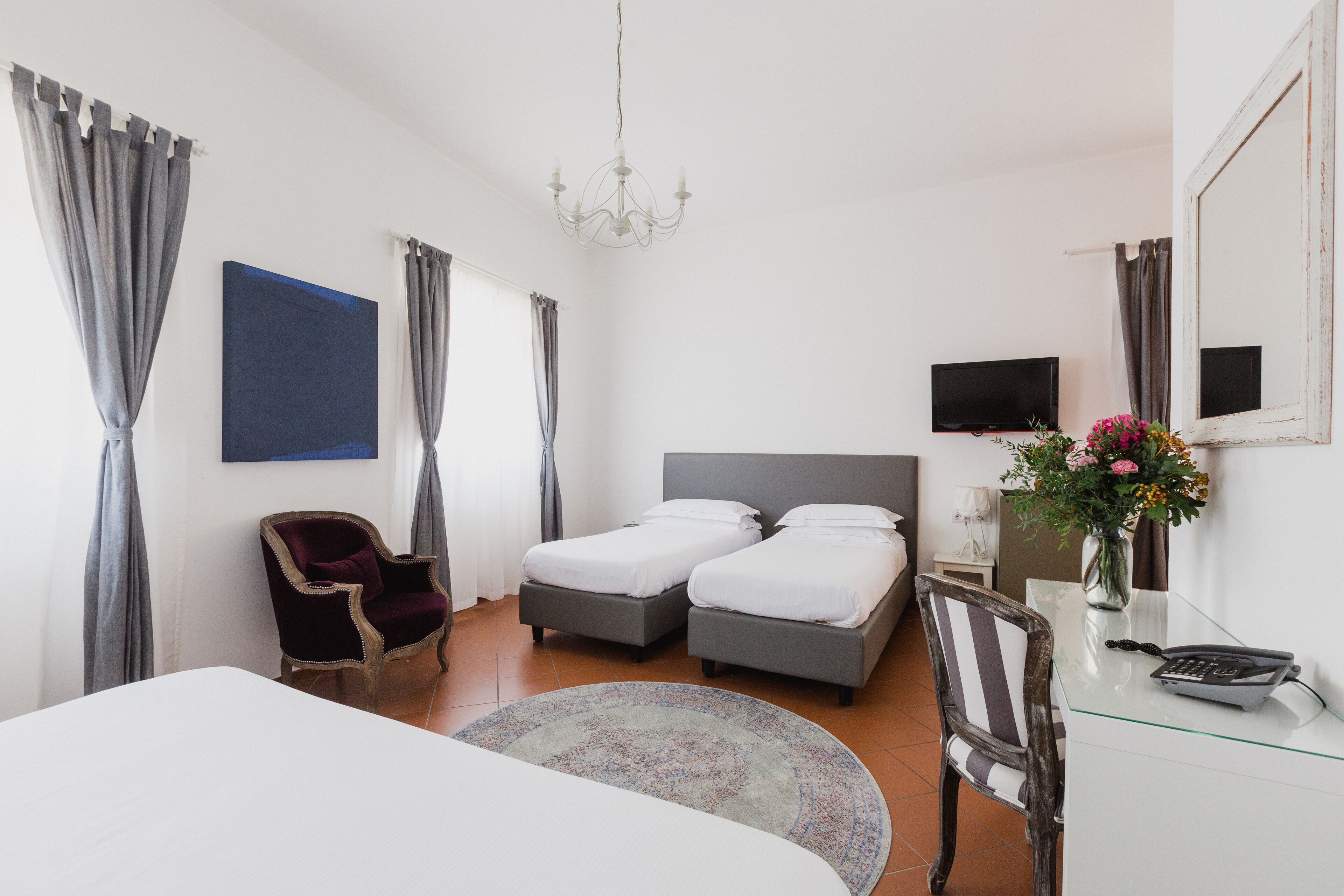Habitación de hotel con dos camas, televisión, escritorio con teléfono, una silla, alfombra y candelabro.