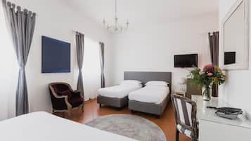 Habitación de hotel con dos camas, televisión, escritorio con teléfono, una silla, alfombra y candelabro.
