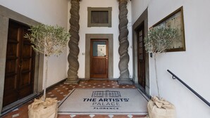 A hallway with a wooden door, two potted plants, and a doormat that reads "The Artists' Palace Florence". - The Artists' Palace Florence (Florence)