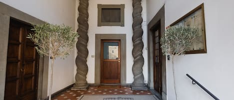 A hallway with a wooden door, two potted plants, and a doormat that reads "The Artists' Palace Florence".