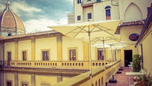 A courtyard with yellow buildings, outdoor seating, and a dome structure in the background. - The Artists' Palace Florence (Florence)