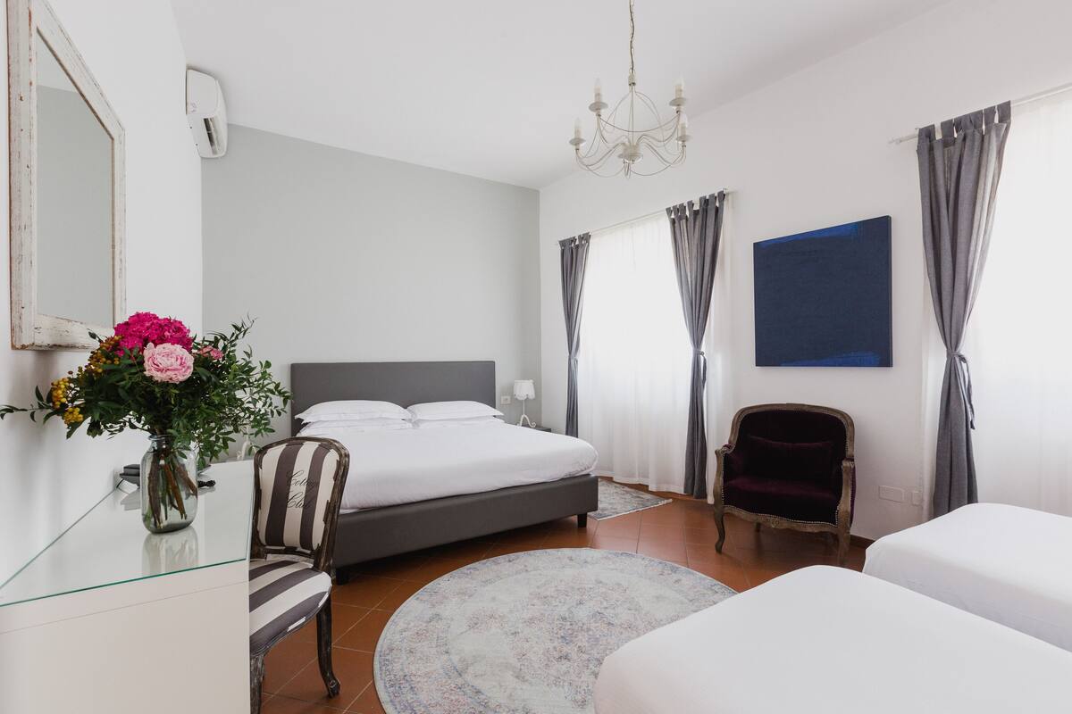A bedroom with a bed, a chair, a desk, and a vase with flowers.