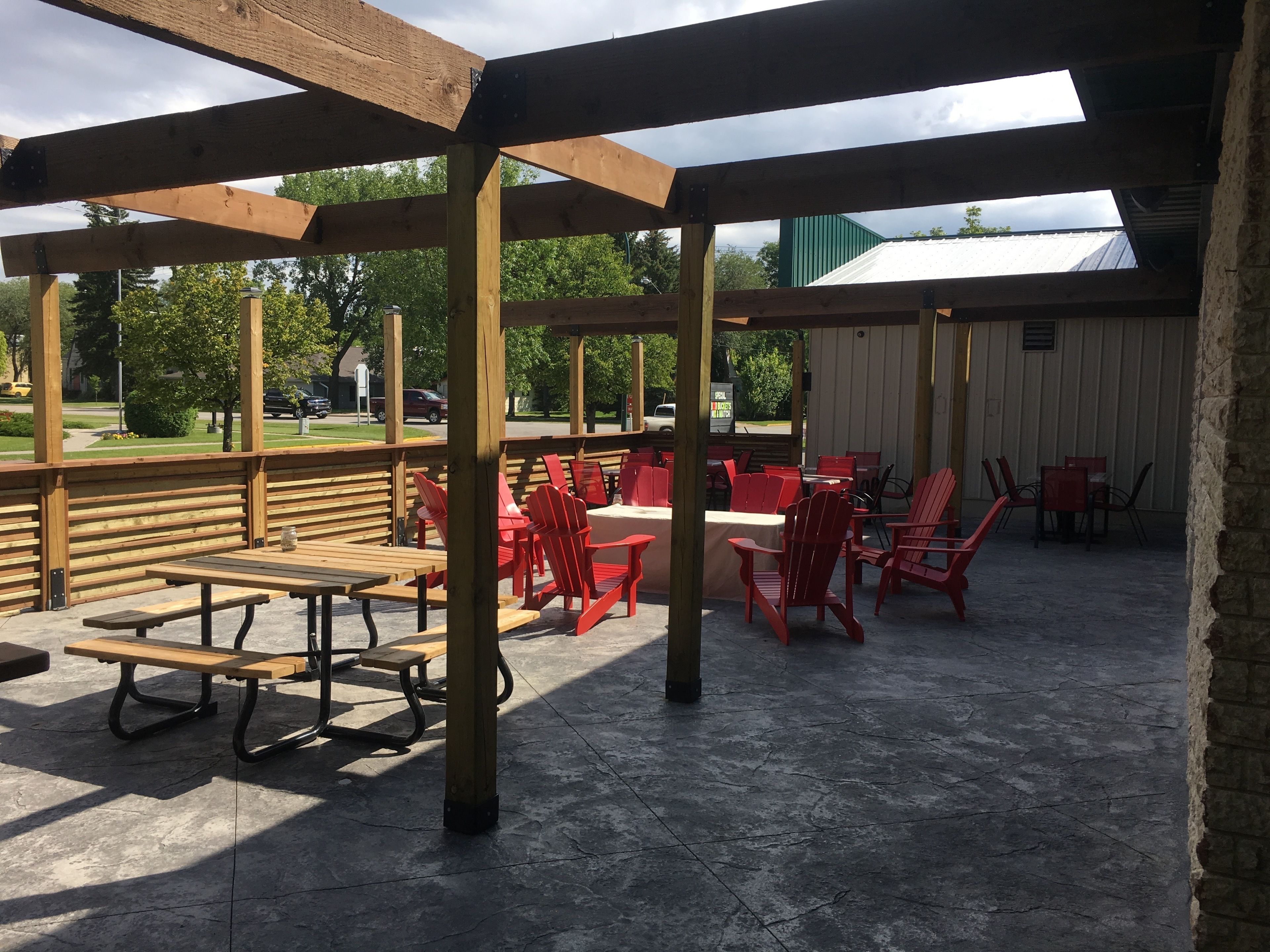 An outdoor patio area with wooden benches and red chairs, a covered section with a view of the surrounding area, and a concrete floor.