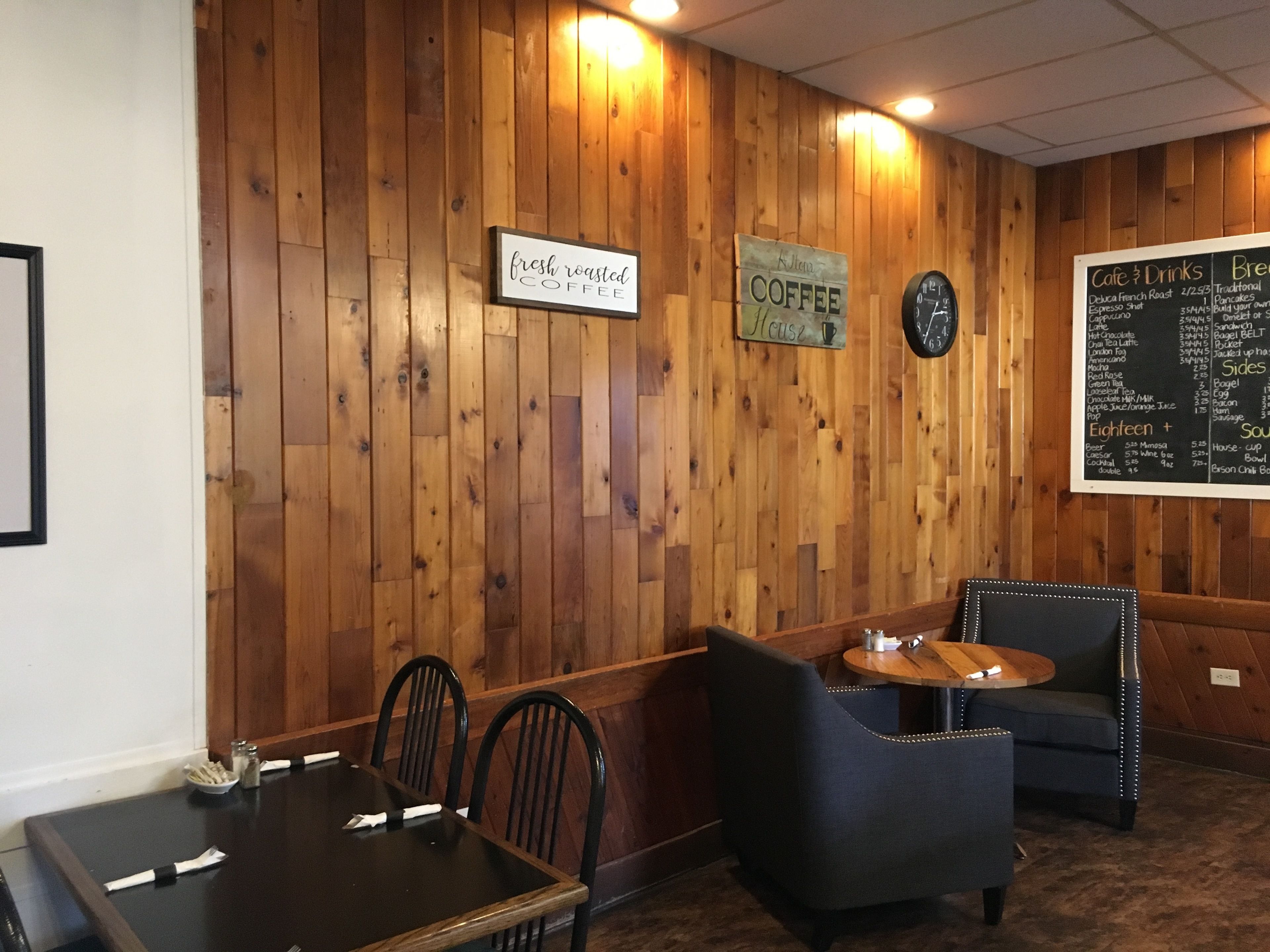 Um café acolhedor com paredes de madeira, um quadro de cardápio e arranjos de assentos.