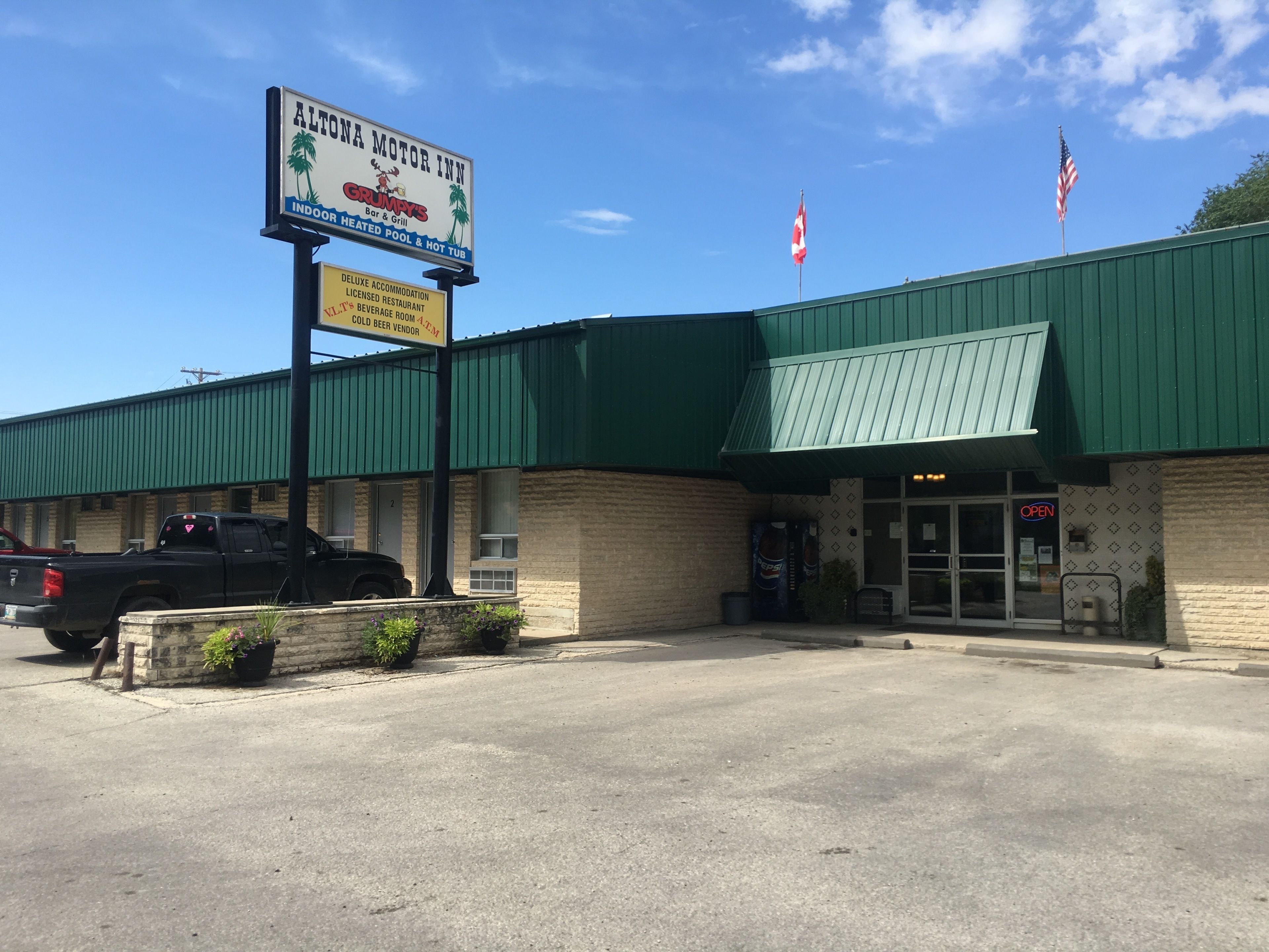 A motel with a green roof, a sign advertising Grumpy's Bar & Grill, and two American flags.