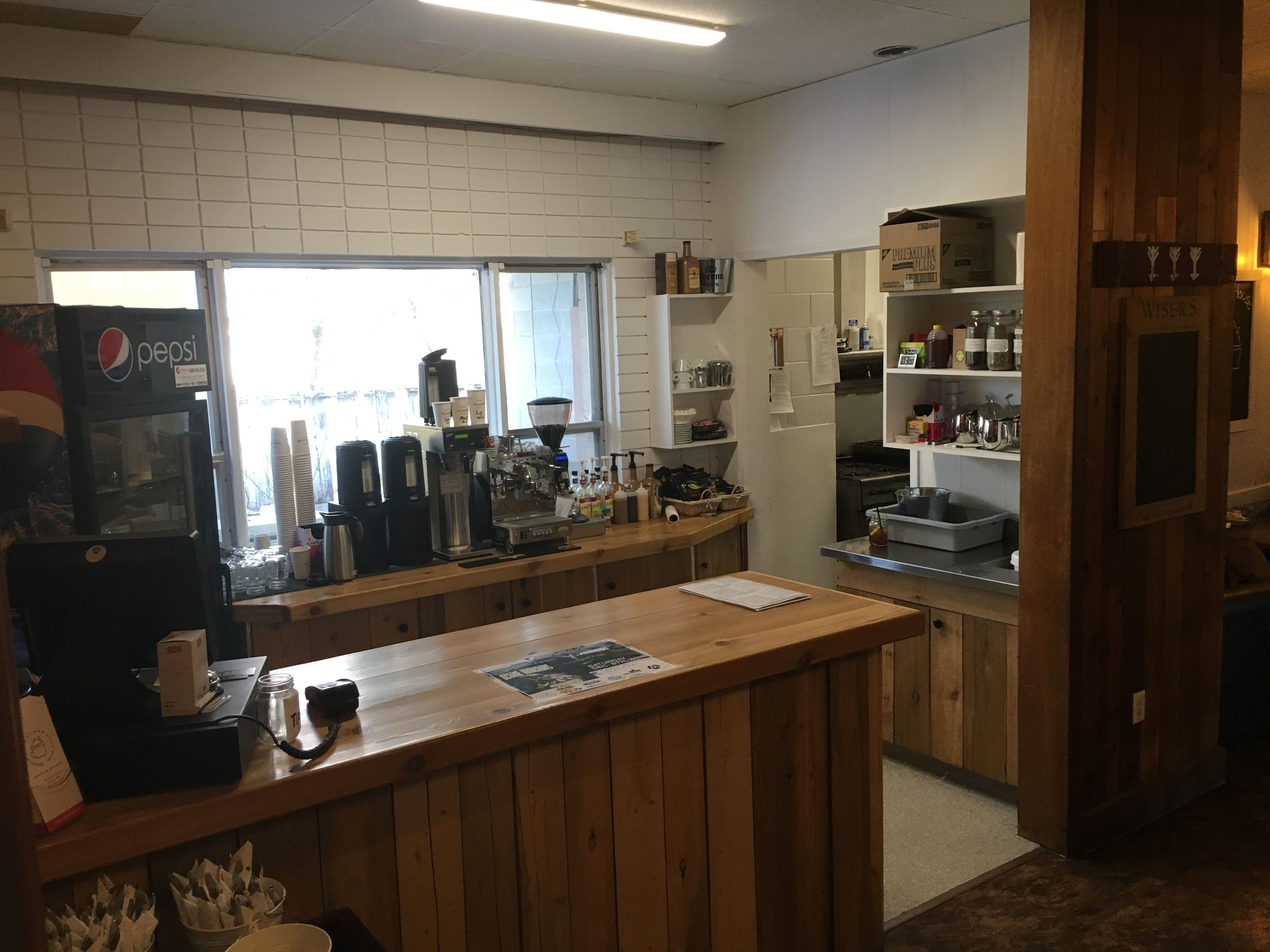 Une cuisine équipée d’une machine à café, d’un réfrigérateur et d’une étagère où sont rangées des bouteilles.