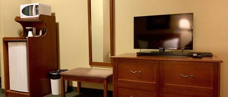 A hotel room with a wooden cabinet, a television, a small refrigerator, a trash bin, and a mirror.