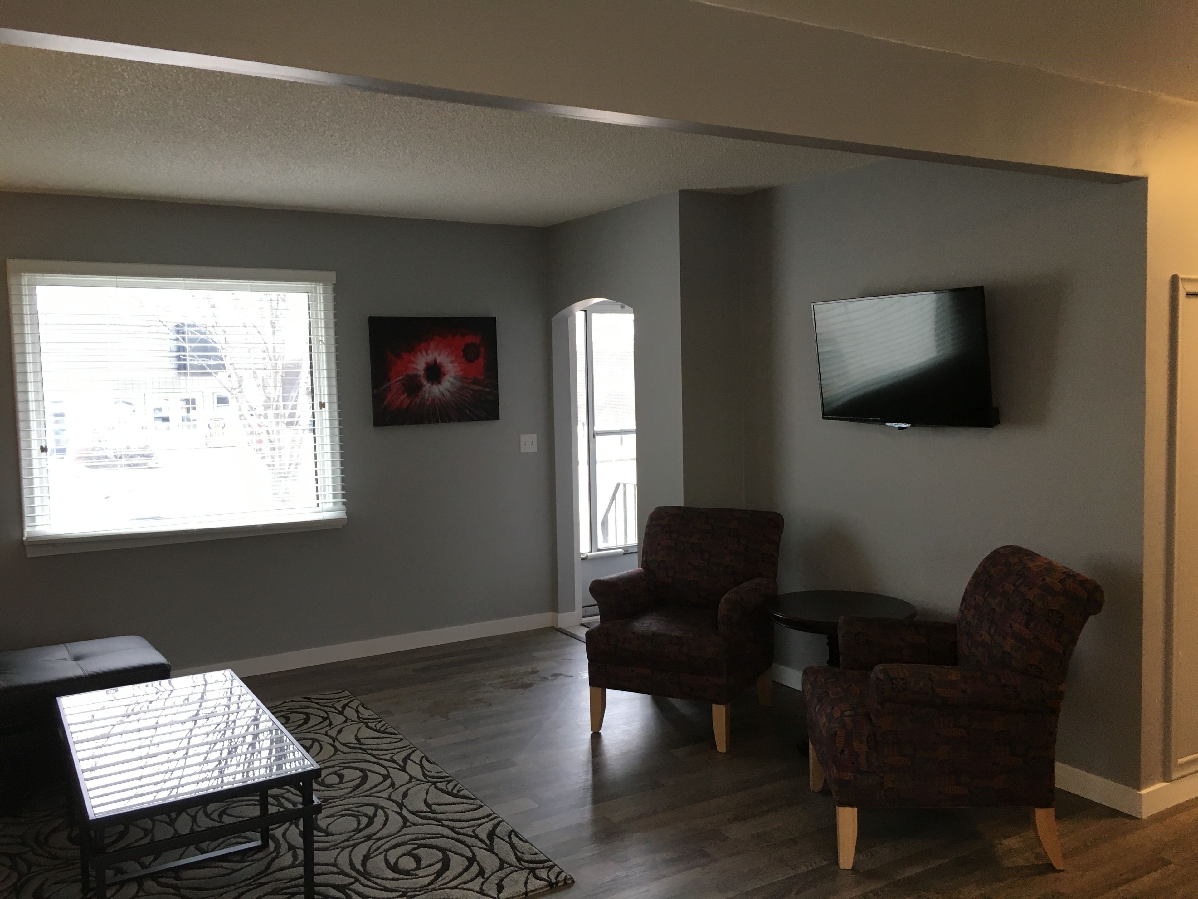 A living room with a large window, a flat-screen TV, two patterned armchairs, a small table, and a patterned rug.