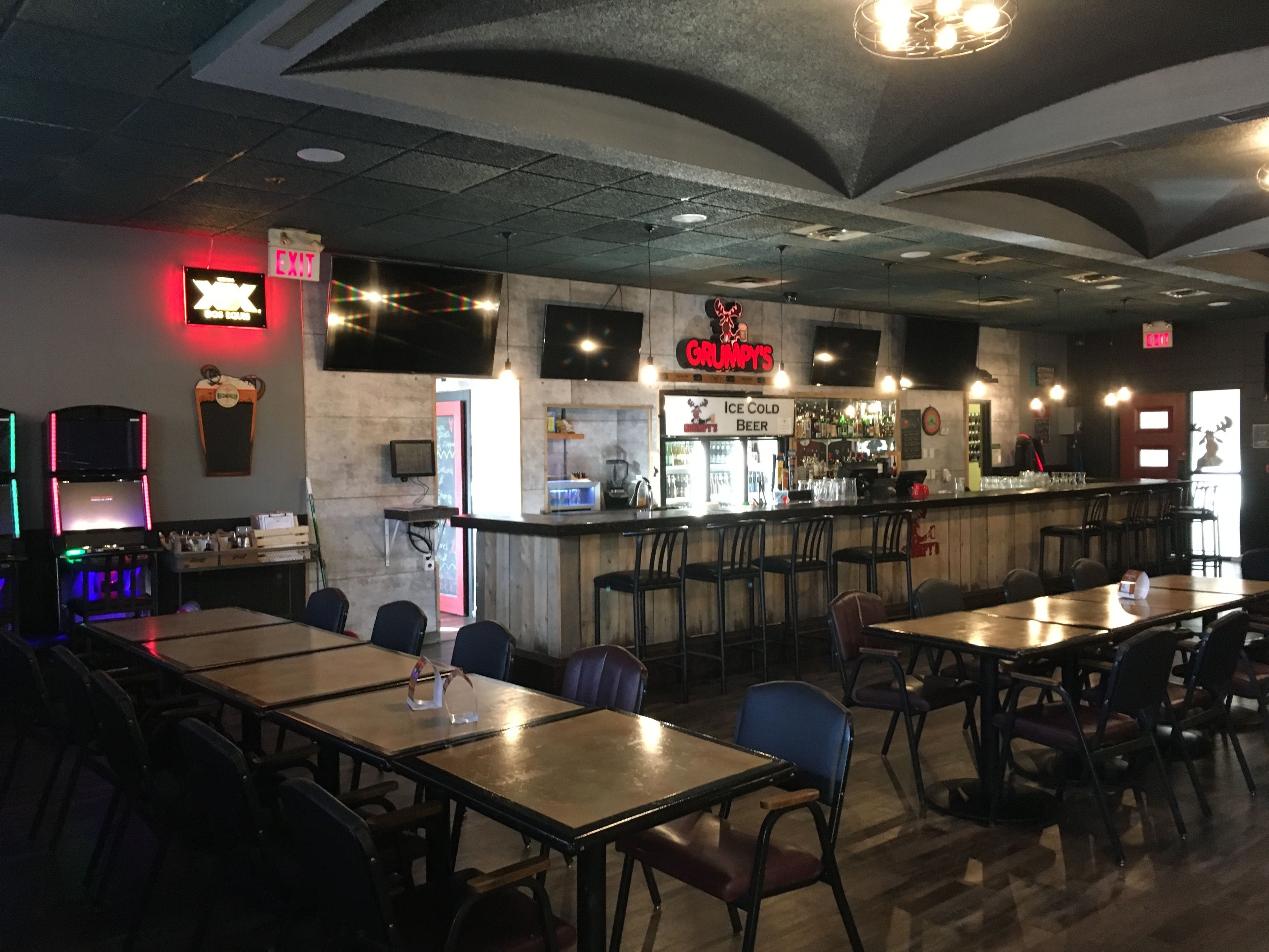 A restaurant interior with tables and chairs, a bar area, and a neon sign for 'Grumpy's'.