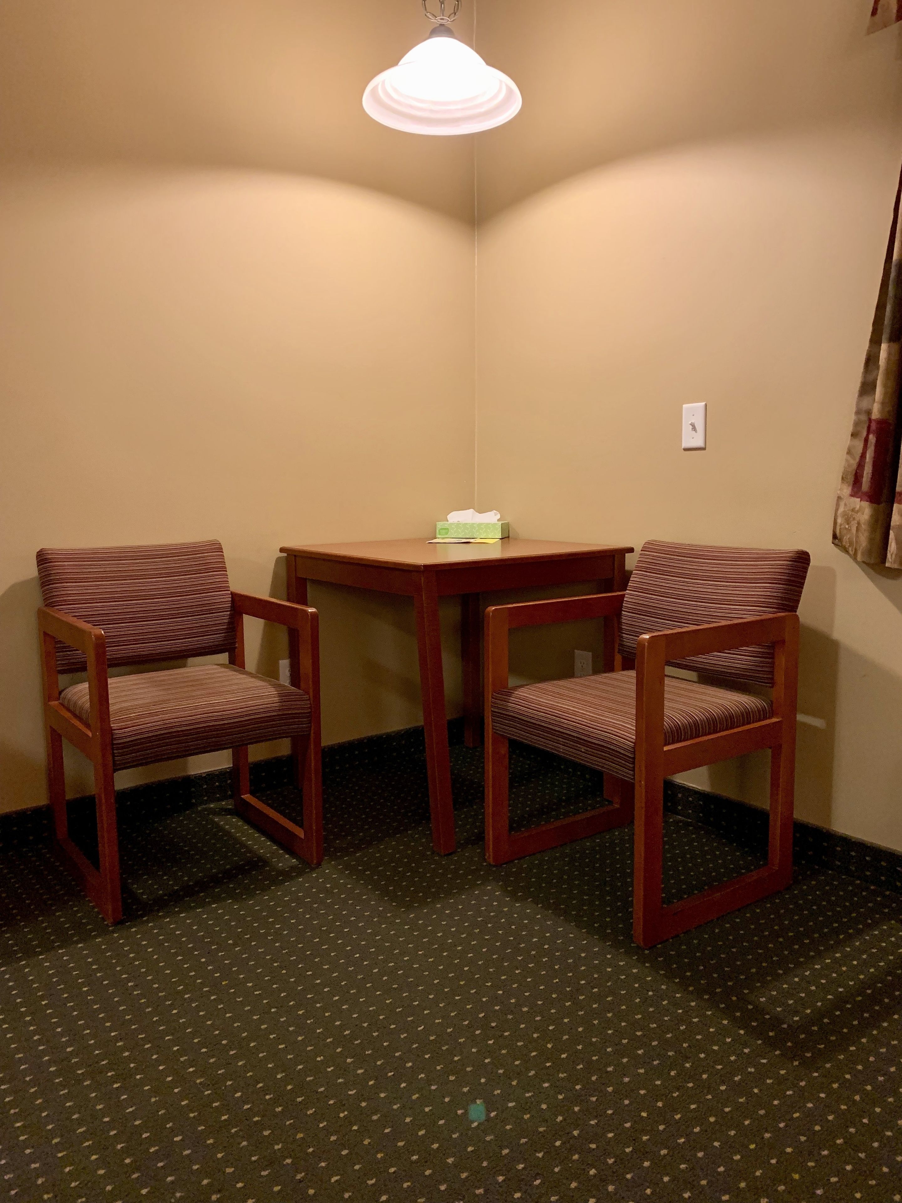 A corner room with two wooden chairs, a small table, and a hanging light fixture.