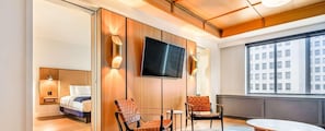 A hotel room with a bed, two chairs, a TV, and a large window with a city view. - Hotel ST Regis Detroit (DETROIT)