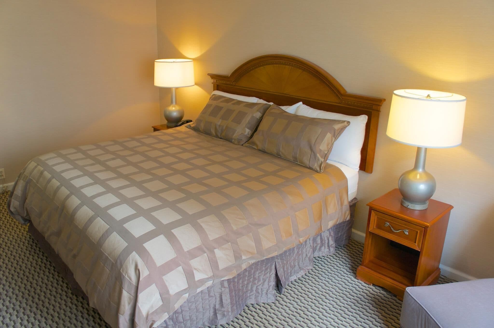 A neatly made bed with a patterned bedspread, two bedside lamps, and a wooden nightstand with a drawer.