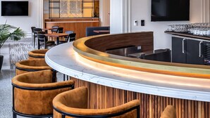 Uma área de bar moderna com balcão curvo, diversas opções de assento e um grande candelabro.