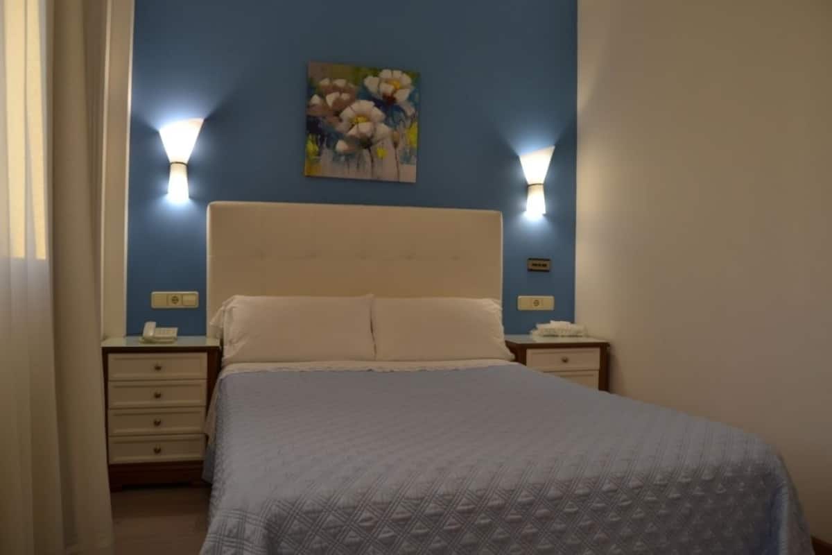 Ein Schlafzimmer mit einem Bett, zwei Nachttischen, einer Wandlampe und einem Gemälde.