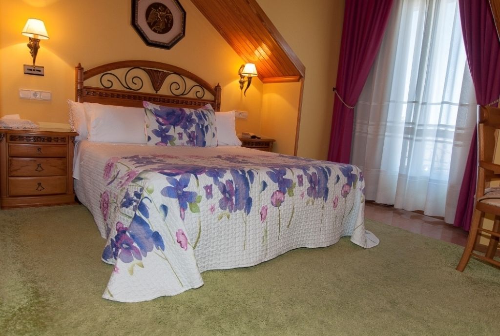 Une chambre à coucher avec une couvre-lit à motifs floraux, une tête de lit en bois, deux lampes de chevet, une table de chevet et une fenêtre avec des rideaux.
