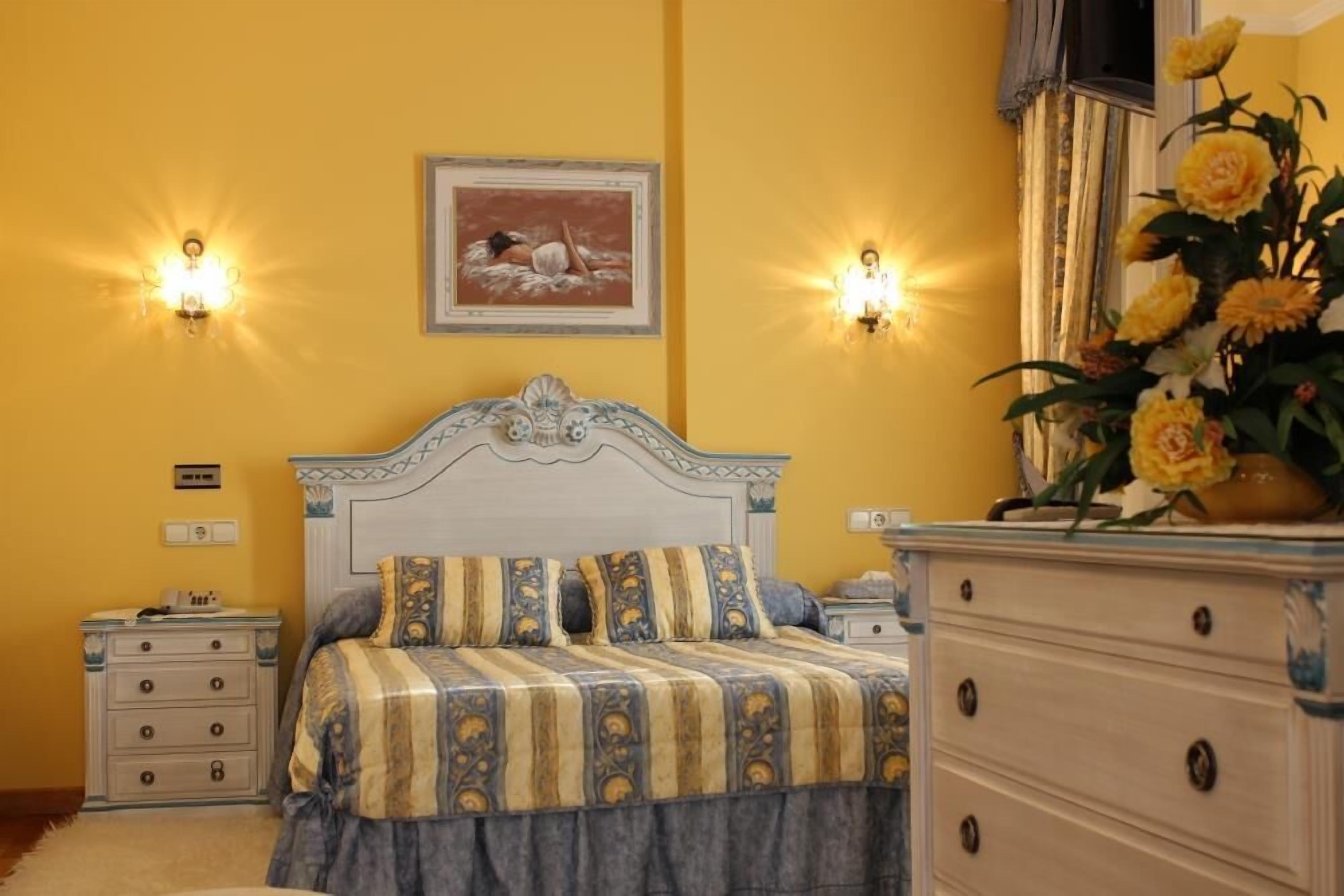A bedroom with a bed, nightstands, a dresser, and wall sconces.