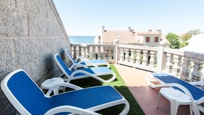 Terraza con sillones azules y una pared de piedra, con vistas a una zona costera con edificios.