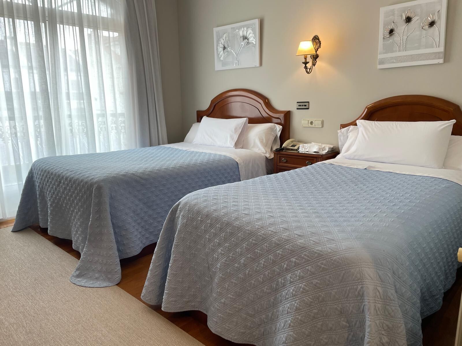 Habitación de hotel con dos camas, una mesita de noche con lámpara y obras de arte en las paredes.