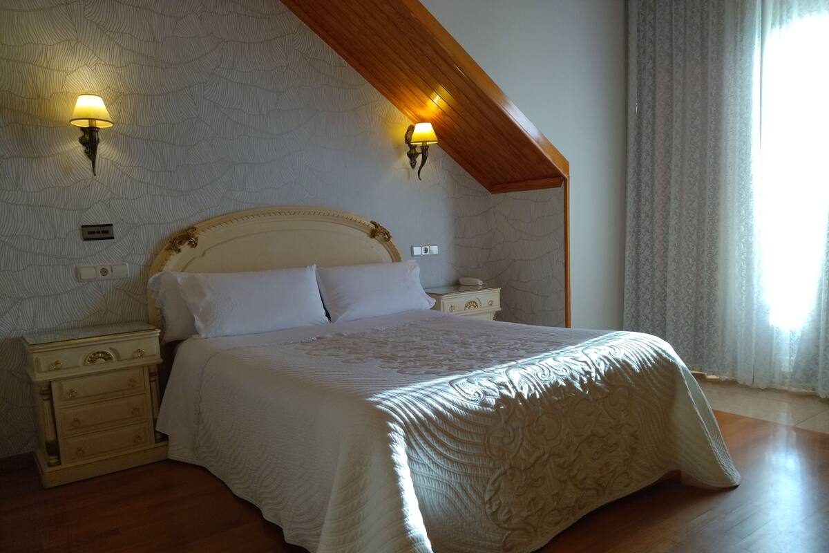 Ein Schlafzimmer mit einem großen Bett, zwei Nachttischen, einer Holzbalkendecke und Wandverkleidung mit Muster.