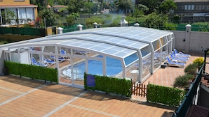 Una piscina cubierta con sillas de descanso, cerramiento de vidrio y zona de patio con baldosas.