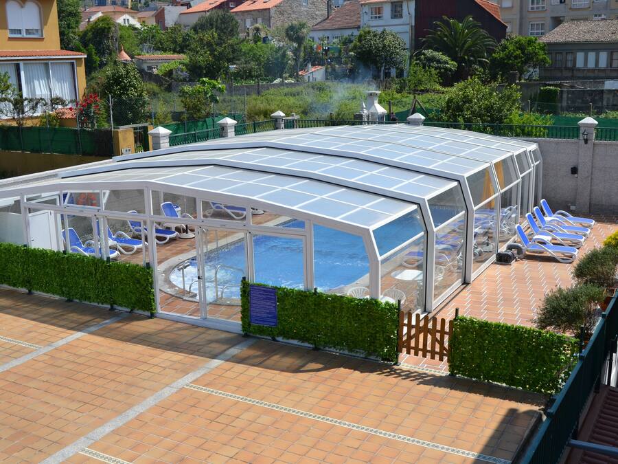 Una piscina coperta con lettini, una struttura in vetro e un patio piastrellato.