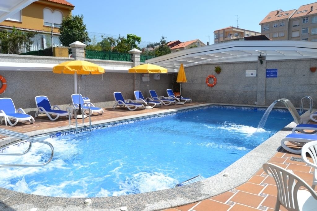 Una piscina con agua azul, rodeada de sillas de descanso y sombrillas amarillas.