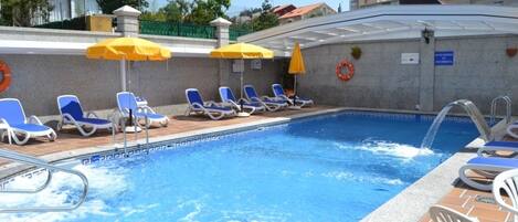 Una piscina con agua azul, rodeada de sillas de descanso y sombrillas amarillas.