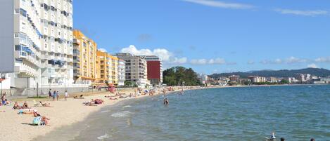 Una playa con varios edificios a lo largo de la orilla, incluyendo un edificio blanco alto y otro naranja más bajo.
