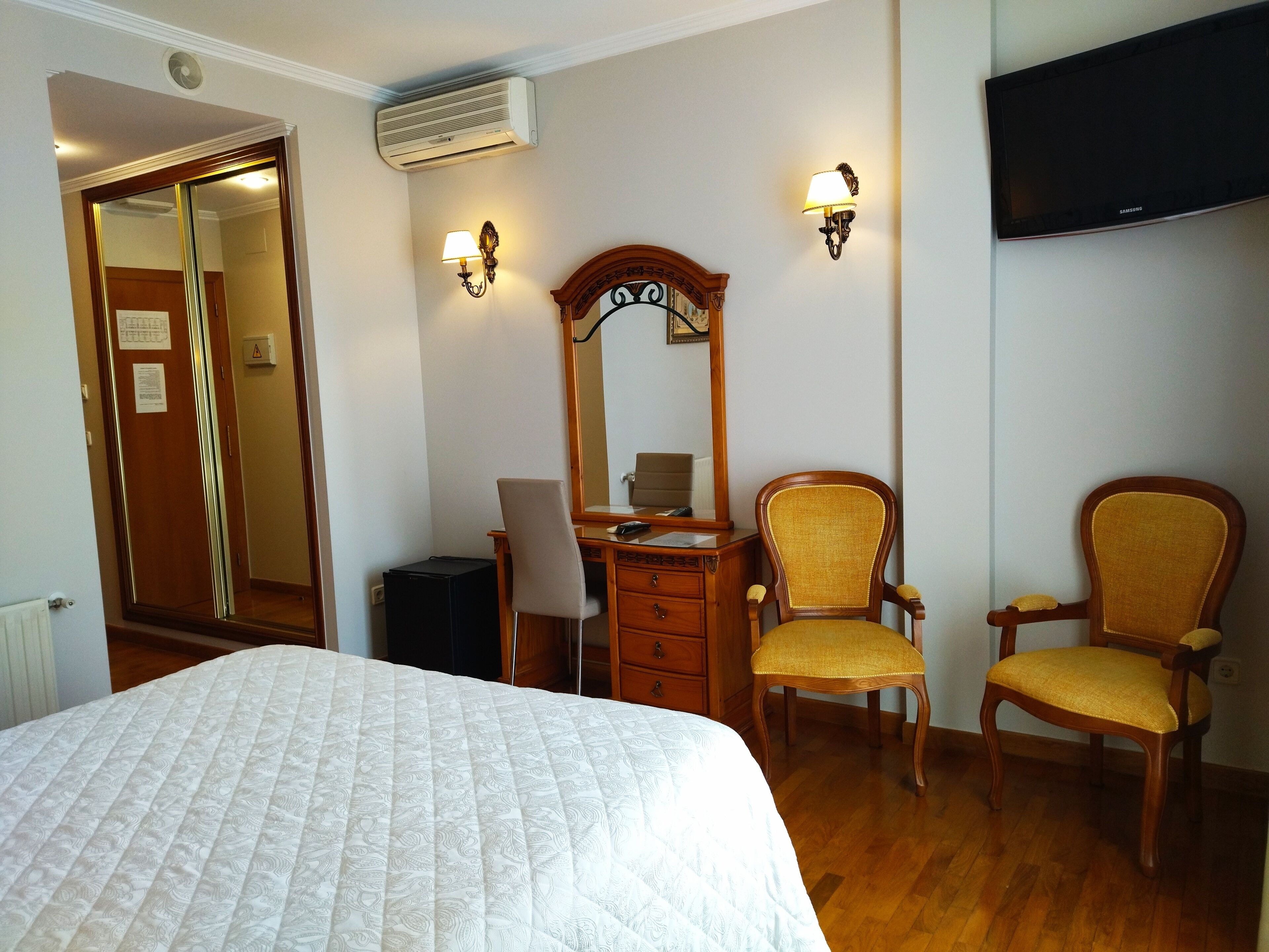 Une chambre d’hôtel équipée d’un lit, d’un bureau, de deux chaises, d’un miroir et d’un téléviseur à écran plat.