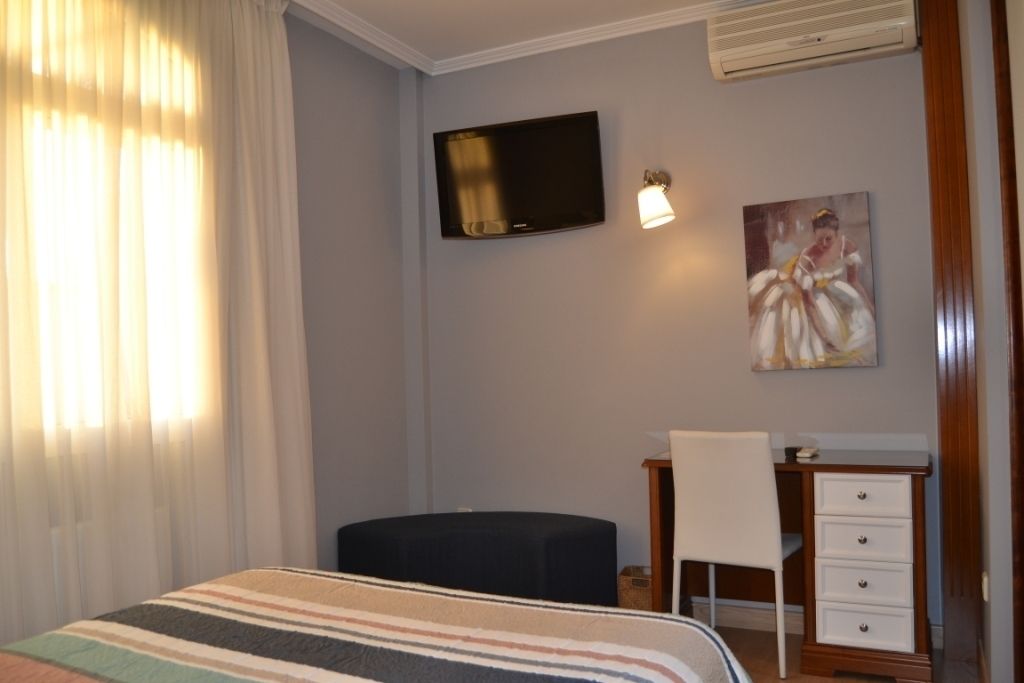 Quarto de hotel com cama, escrivaninha com cadeira, televisão e um quadro na parede.