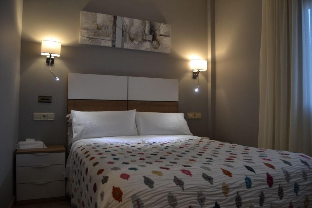 Una habitación de hotel con una cama, dos mesitas de noche, una obra de arte en la pared y dos apliques.