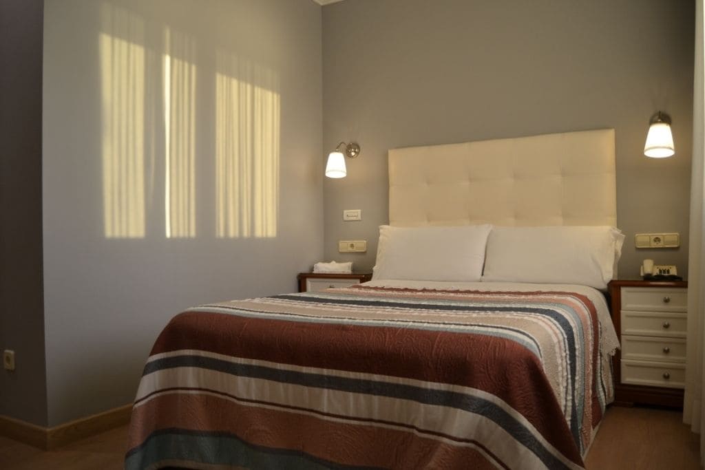 A bedroom with a bed, nightstands, a dresser, and a window with curtains.