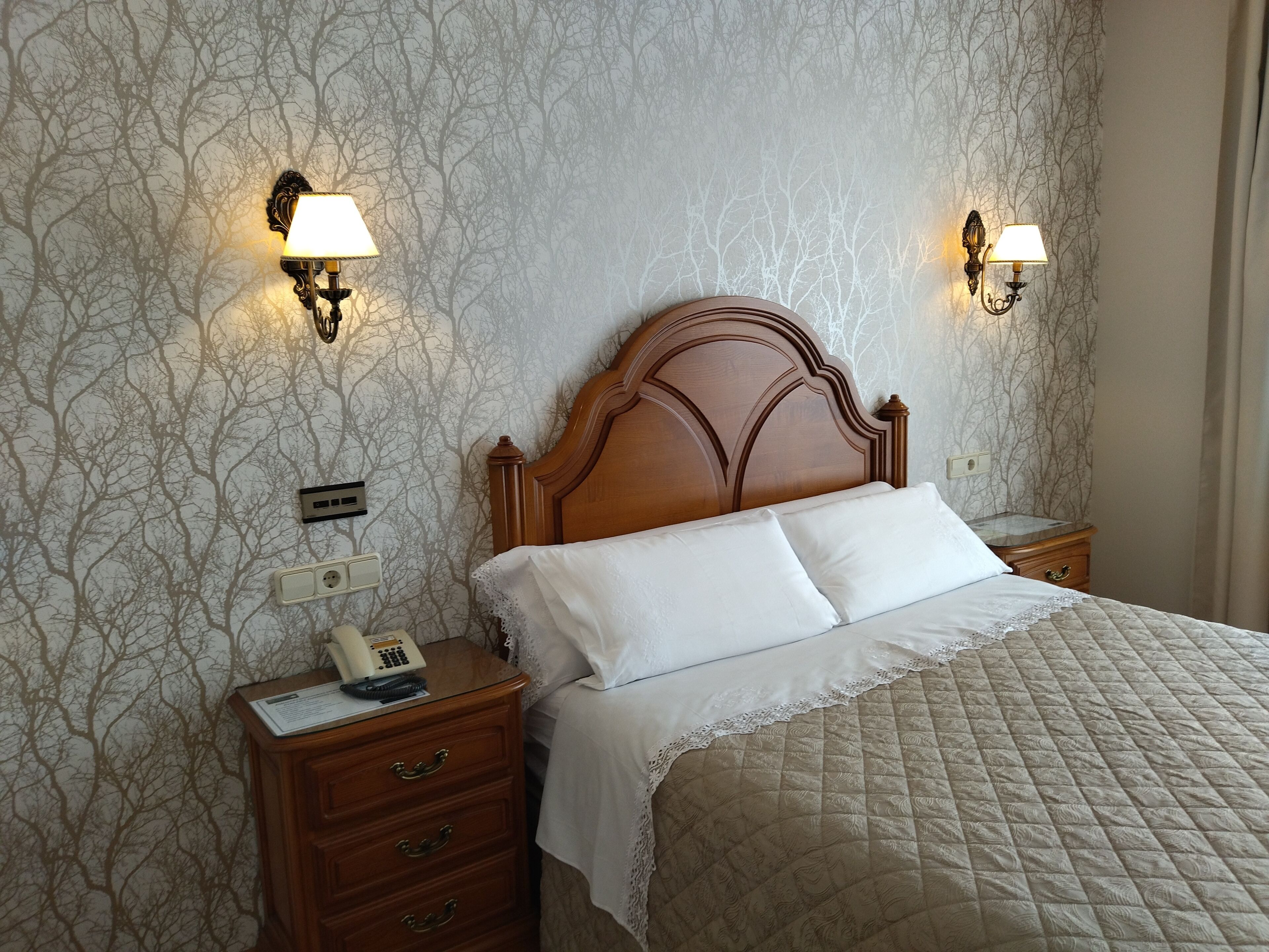 A neatly made bed with a wooden headboard, two bedside lamps, and a nightstand with a telephone.
